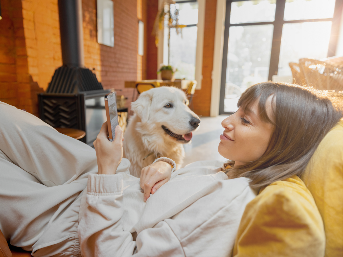 Μια γυναίκα που κοιτάει το κινητό της στον καναπέ της αγκαλιά με τον σκύλο της 