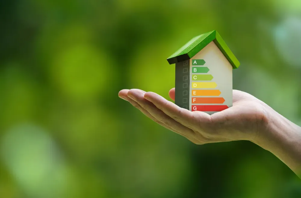 ένα χέρι που κρατάει στην παλάμη του ένα σπίτι που είναι ενεργειακά αποδοτικό, σε ένα πράσινο φόντο