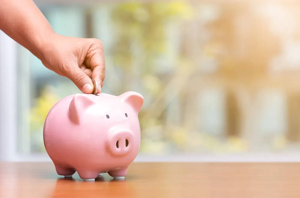 κουμπαρά γουρουνάκι και ένα χέρι που βάζει ψιλά, υποδεικνύοντας οικονομία